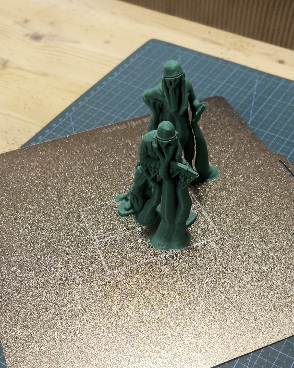 Two green PLA army men on the print plate, still standing in their tree supports