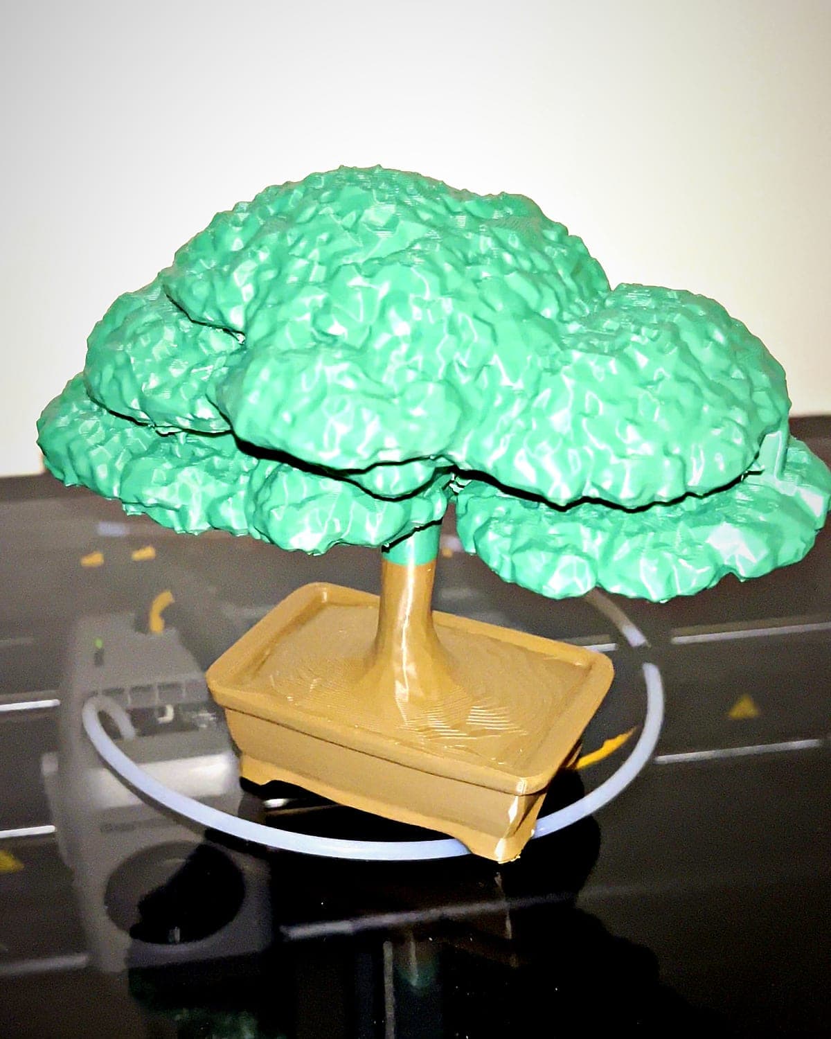 Two-colour 3D-printed bonsai tree with a mint green canopy and a tan pot, on top of the printer