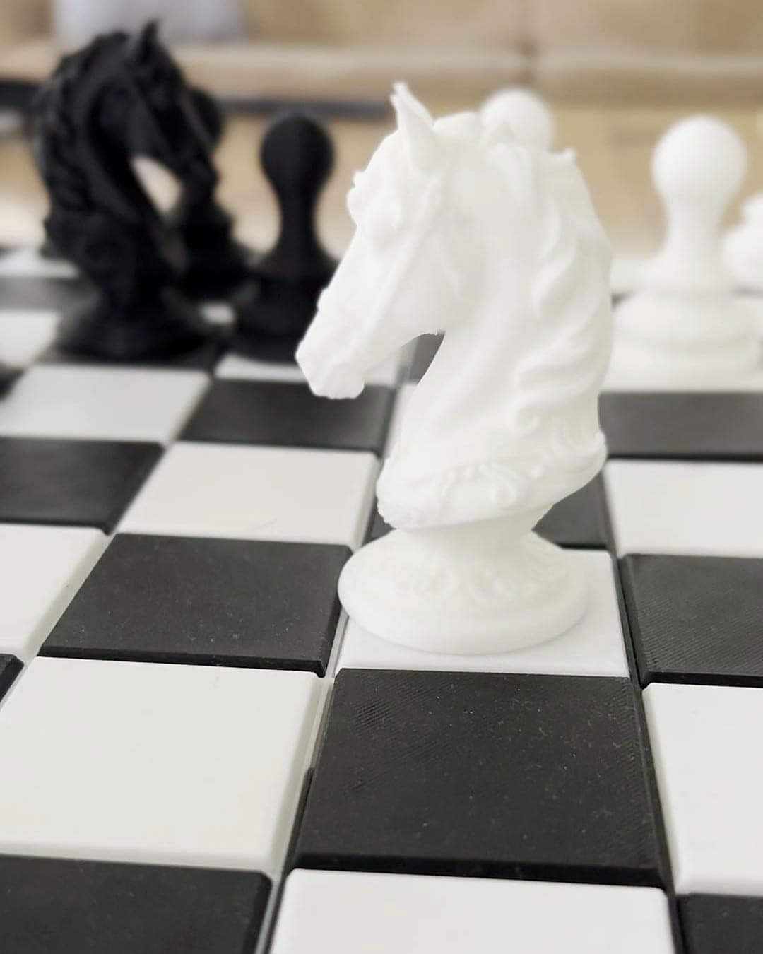 White PLA chess knight with a carved mane on a printed black and white board, black pieces behind
