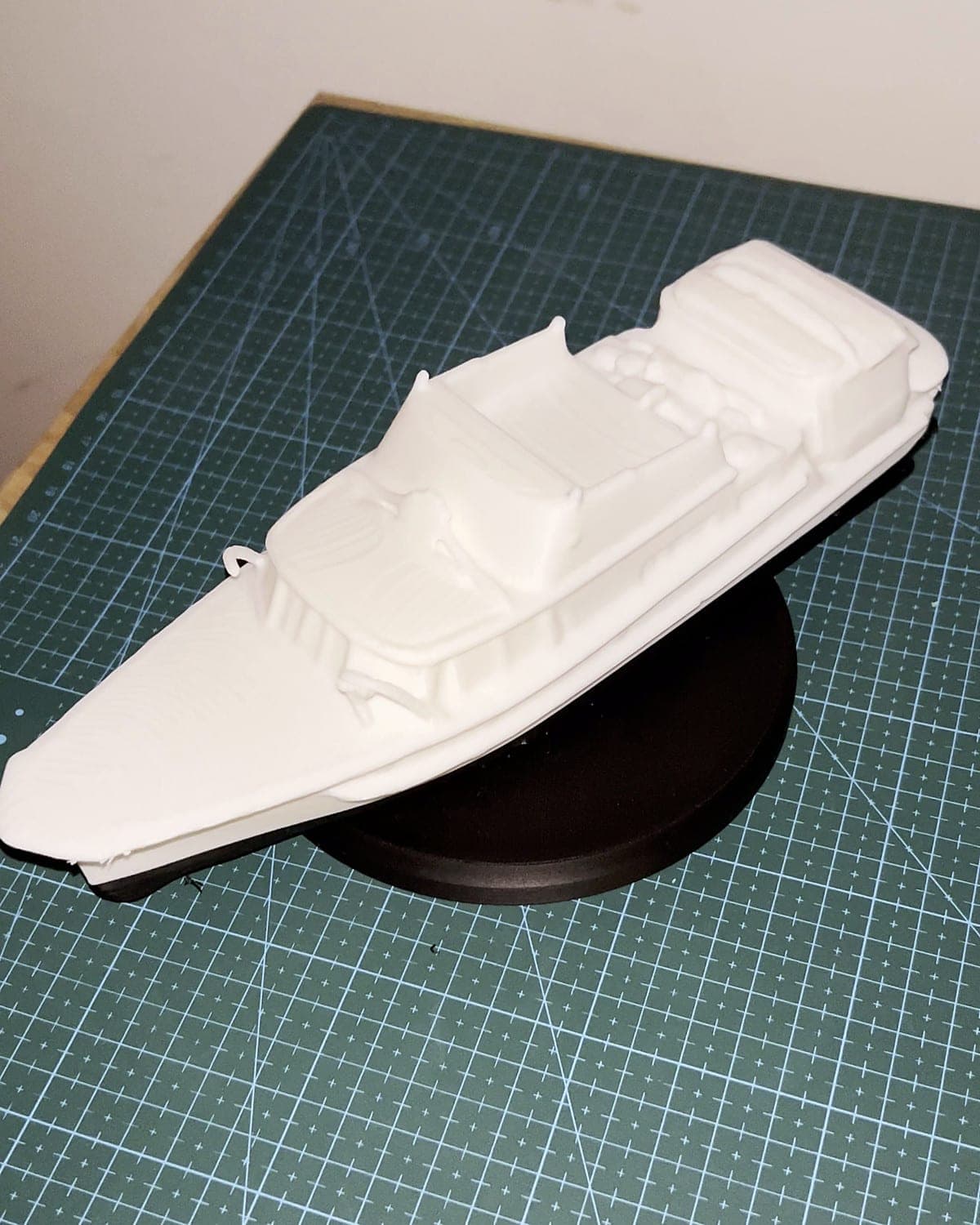 White 3D-printed model of a motor launch on a round black display stand, on a green cutting mat