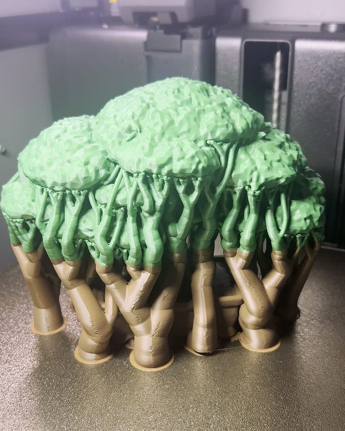 A two-colour bonsai print on the textured print bed, its green canopy still standing on a forest of tree supports