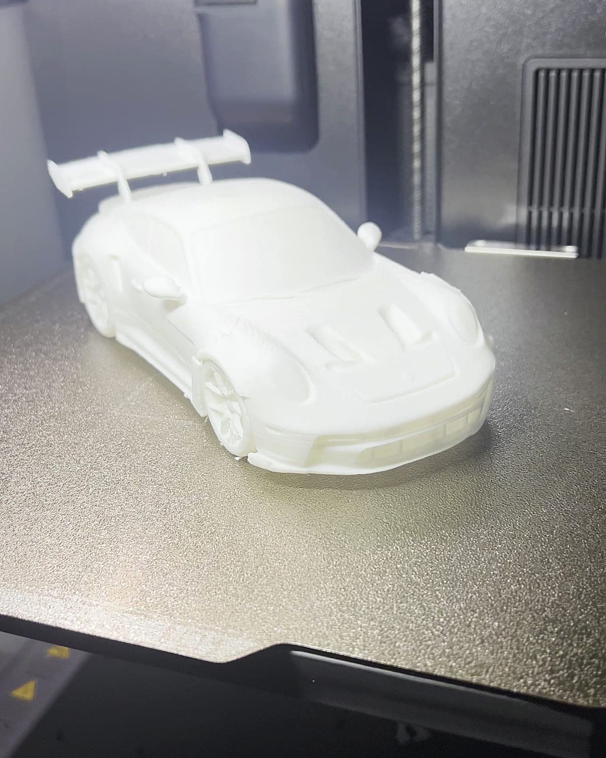 White 3D-printed sports car model on the print bed inside our printer in Tauranga, just finished