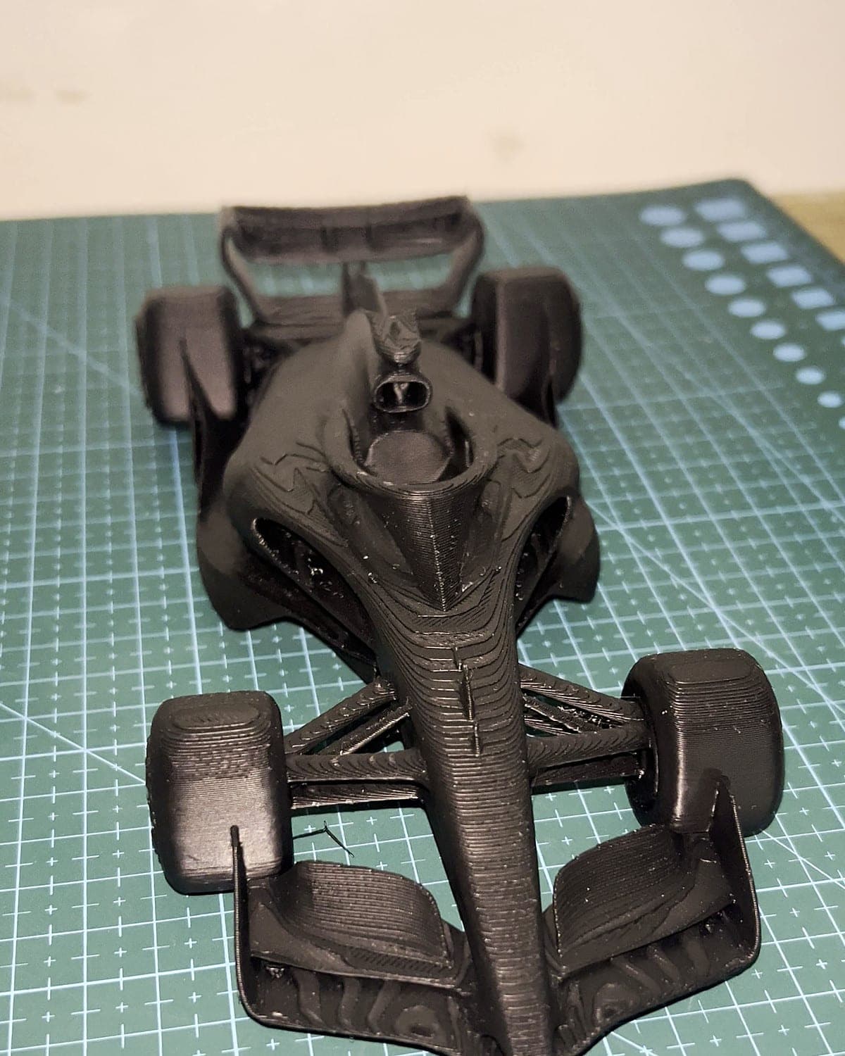 Black 3D-printed model of an open-wheel race car on a green cutting mat